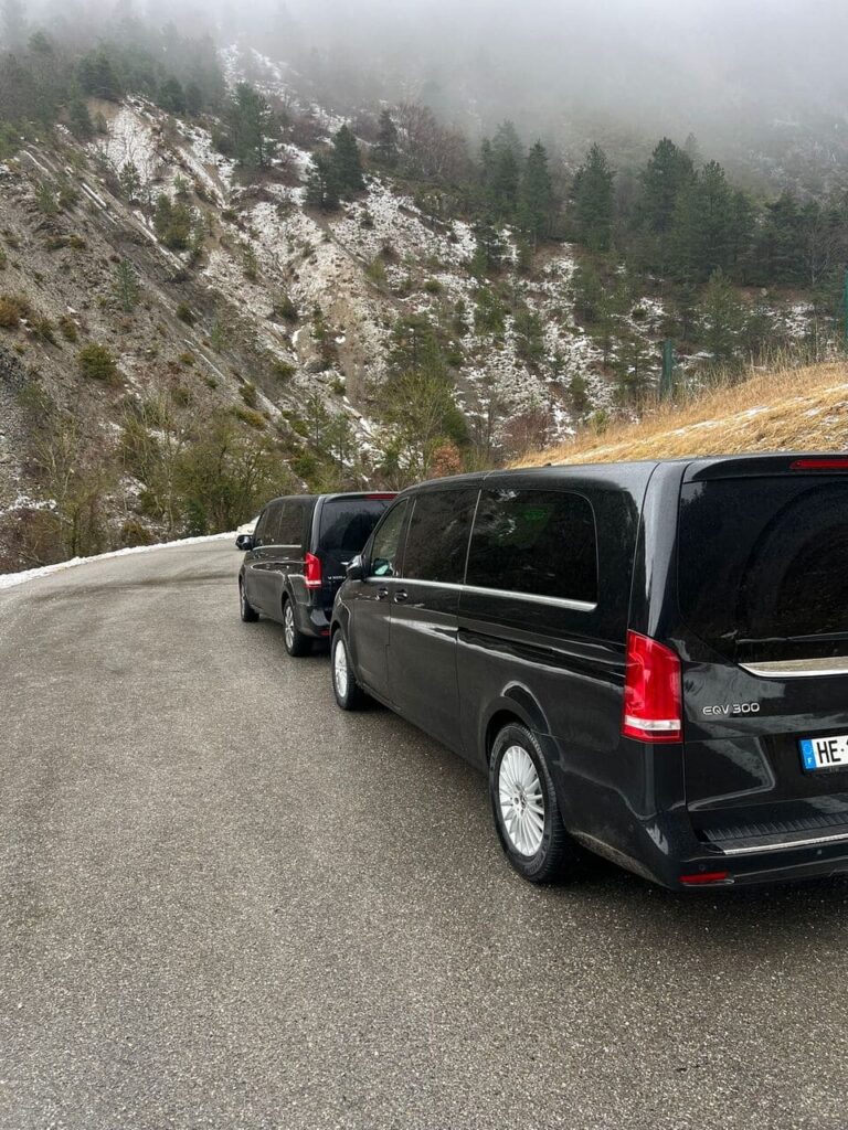 deux minibus noirs stationnés sur une route asphaltée bordant une montagne enneigée recouverte de pins et de brouillard.