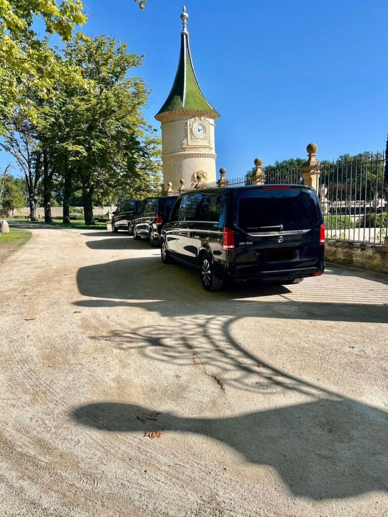 Une file de vans noirs stationnés sur un chemin de gravier, devant un château avec une tour à toit vert.Chauffeur VTC Pour L'événementiel