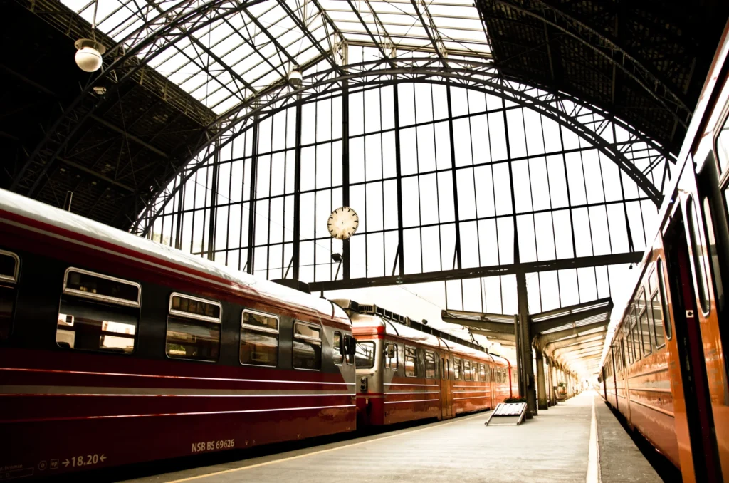 Trains rouges côte à côte sur le quai d'une gare avec une grande verrière et une horloge murale.