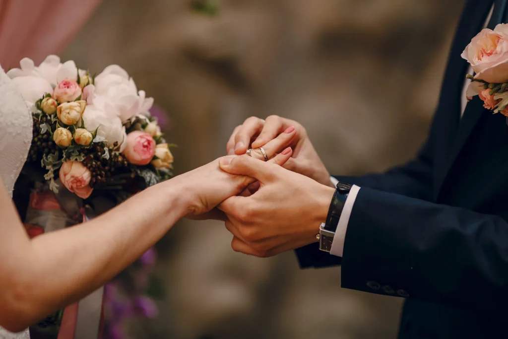 Un homme en costume à un mariage met une alliance au doigt d'une femme à côté d'un bouquet de roses roses et blanches.